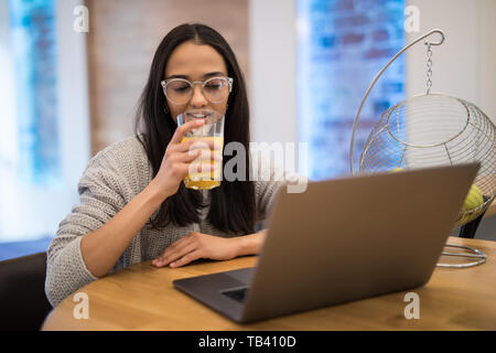 Portrait of beautiful caucasian woman using laptop at table in kitchen interior while having breakfast at home Stock Photo
