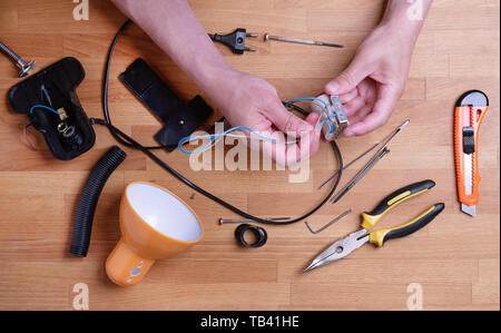 Man fixing desk lamp wires top view. Electrician repairing lights. Technician service workplace concept. Tools and instruments on table. Male hands holding electronic broken parts, details Stock Photo