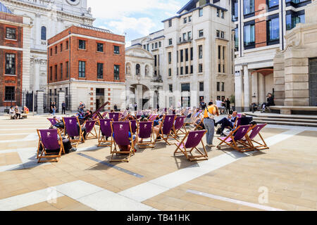 Tourists and local office workers sitting in purple deckchairs in Paternoster Square in the City of London, UK Stock Photo