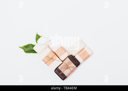 Organic natural handmade soaps of various types wrapped in brown paper next to green leaves on white background, flat lay. Stock Photo