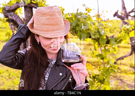 Girl with a glass of red wine in the green vineyards at sunset. Beautiful nature and girl. Copy space Stock Photo
