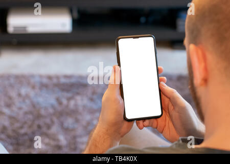 A white male middle aged male sat down in living room looking at his mobile phone Stock Photo