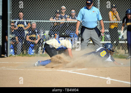 Catcher applying a tag to a sliding runner attempting to score as the home plate umpire looks on in advance of making a call. USA. Stock Photo