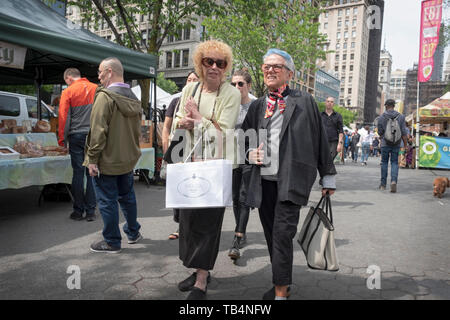 Two youthfull looking middle age women walk through the Union Square Green Market chatting and holding shopping bags. In New York City. Stock Photo