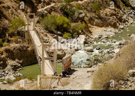 Hikers resting on the trail next to the suspension bridge to cross the Colca River at the Colca Canyon, Cabanaconde District, Peru Stock Photo