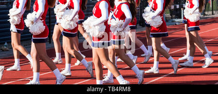 High school cheerleaders in red, white and blue uniforms cheering to the fans in the stands during a homecoming football game. Stock Photo