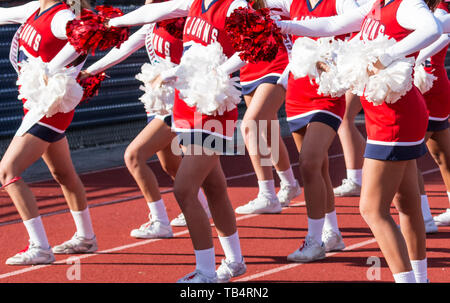 A high school cheerleader squad with red and white pom poms are cheering on the sidelines during their homecoming football game. Stock Photo