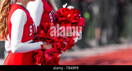 Two high school cheerleaders with red and white pom poms at a football game in autumn. Stock Photo