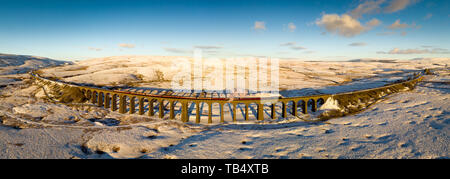 Aerial panorama of the steam train passing over Ribblehead Viaduct on the Settle Carlise Railway, in Snowy Yorkshire Dales Scenery