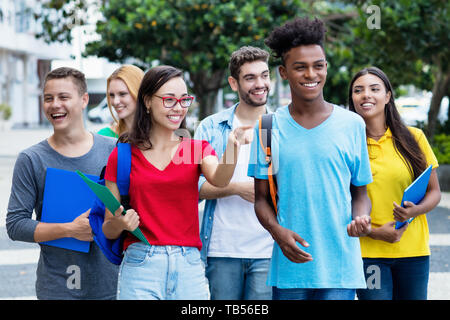 French female student and african american guy with group of mutliethnic students outdoor in city in summer Stock Photo