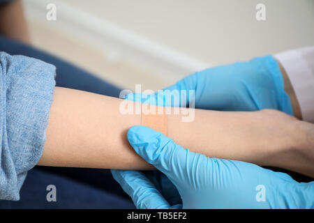 Doctor applying plaster onto hand of young woman, closeup Stock Photo