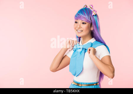 Smiling otaku girl in purple wig looking away isolated on pink Stock Photo