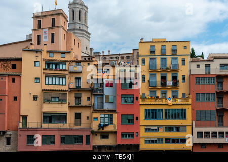 Multi colored houses and spire of Collegiate Church of Sant Felix from bank of the Onyar River, Girona, Spain. Estelada Blava, flag of Catalonian inde Stock Photo