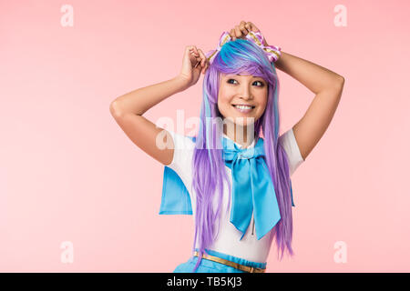 Smiling asian otaku girl in purple wig standing on pink Stock Photo