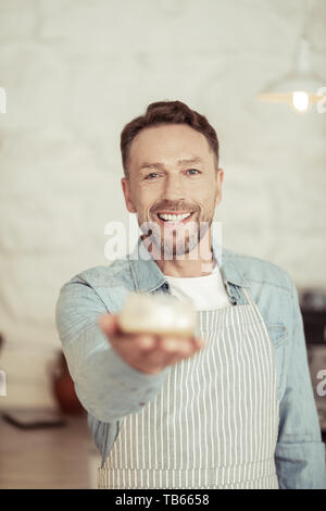 Drink it. Smiling handsome barista putting his hand out suggesting a cup of fresh fragrant coffee. Stock Photo