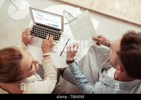 Reading documents. Two smiling business partners sitting by the laptop and working together in a cafe. Stock Photo