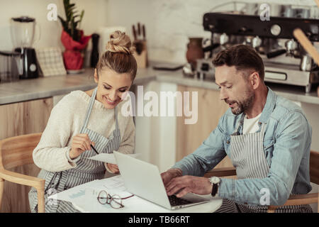 Working with a smile. Two smiling concentrated people sitting at the cafe table working on their common project. Stock Photo