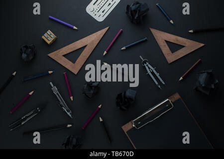 Black on black flat lay pattern with a clipboard, eraser shield, pencils, and rulers. Drawing blueprints header with copy space. Stock Photo