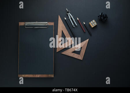 Black on black flat lay with a clipboard, pencils, and rulers. Drawing blueprints header with copy space. Stock Photo