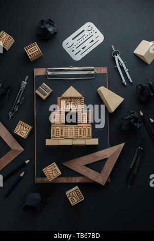 House construction, planning, and repairment concept. Wooden block home on a clipboard with engineering equipment, compasses, rulers and pencils. Stock Photo