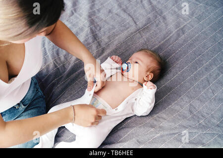 Mom dresses a newborn baby, buttoning up a jumpsuit. Home comfort Stock Photo
