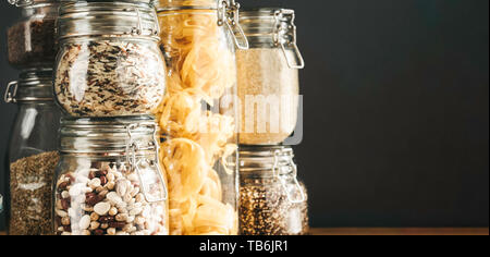 Banner with assortment of uncooked grains, cereals and pasta in glass jars on wooden table. Healthy cooking, clean eating, zero waste concept. Balance Stock Photo
