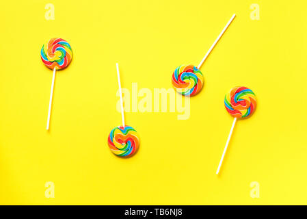 Round colorful lollipops on yellow background. Top view. Confetti for holidays, birthday party concept. Stock Photo