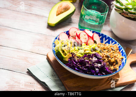 Buddha bowl with rainbow colors ingredients - avocado, fermented red cabbage, quinoa, radish, green beans, sesame and pumpkin seeds. Dish served on wo Stock Photo