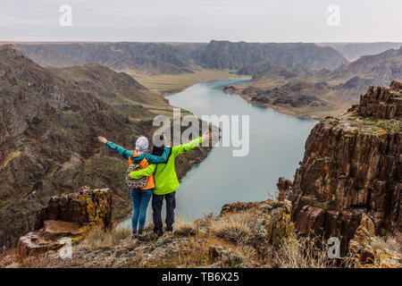 A pair of young people looking at a landscape with a river, they stand on the edge of the cliff. Back view. Spring landscape. Ili River. Kazakhsta Stock Photo
