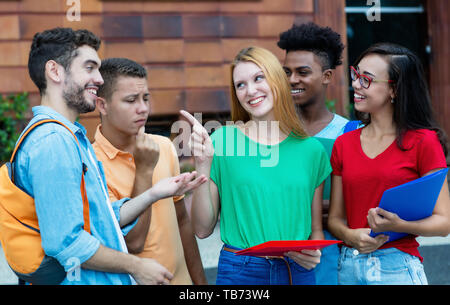 Group of caucasian and latin and african american students talking about homework outdoors in summer Stock Photo
