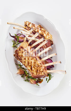 Dual portion serving of roasted rack of lamb with trimmed bone-in chops served with fresh rosemary, roast garlic and onion viewed top down on white Stock Photo