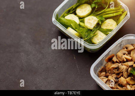 The food in the containers, a healthy diet, good nutrition concepts. Mushrooms, fresh herbs dill, parsley, onions, spinach and cut pieces of cucumbers Stock Photo