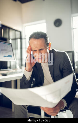 Mature interior designer looking at sketches having headache Stock Photo