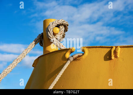 Detail of a yellow mooring bollard with ropes or hawsers on the deck of a ship moored in the port Stock Photo