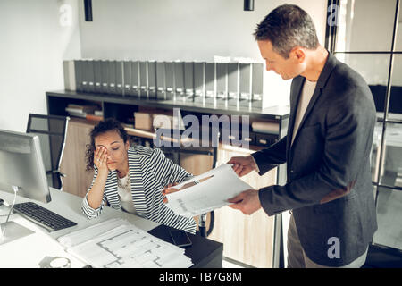 Dark-haired secretary feeling tired and sleepy talking to boss Stock Photo