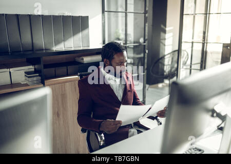 Bearded dark-skinned businessman reading documents in office Stock Photo