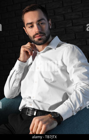 Handsome fashionable man sitting in armchair against dark background Stock Photo