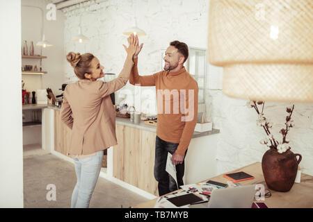 Friendly atmosphere. Two happy colleagues smiling and high-fiving each other standing in the kitchen. Stock Photo