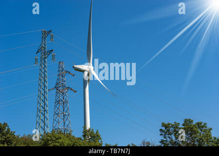 Wind turbine and high voltage towers (power line) on a clear blue sky with sun rays - Renewable energy concept