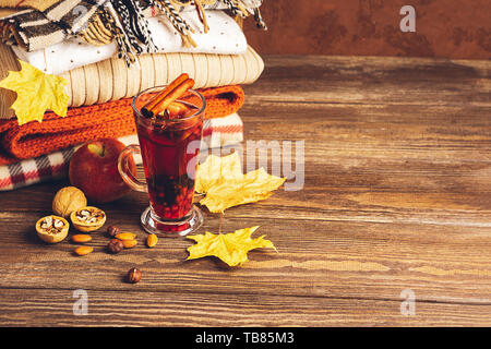 Hot drink of apples and berries, sangria in a glass and a stack of knitted clothes on a wooden background. Autumn concept. Copy space. Selective focus Stock Photo