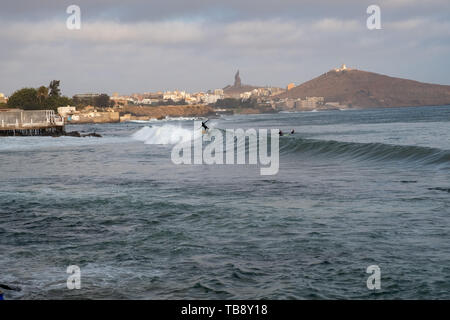 People surf on a beach in Dakar, Senegal, with the African Renaissance Monument and Mamelles lighthouse in the background. Stock Photo