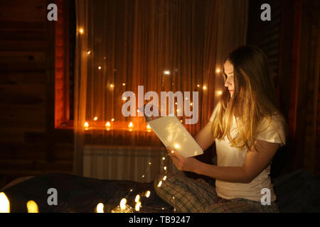 Beautiful woman reading fairy tales in darkness with glowing lights Stock Photo