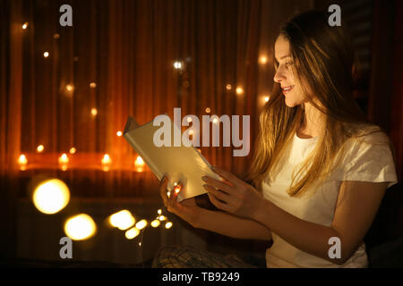 Beautiful woman reading fairy tales in darkness with glowing lights Stock Photo