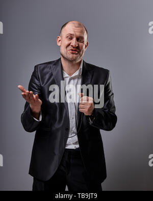 Fun emotional moving happy performer man presenting the show holding microphone in hand and showing the hand the welcome sign on grey color background Stock Photo