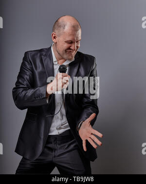 Smiling emotional moving happy performer man presenting the show holding microphone in hand on grey color background. Closeup portrait Stock Photo