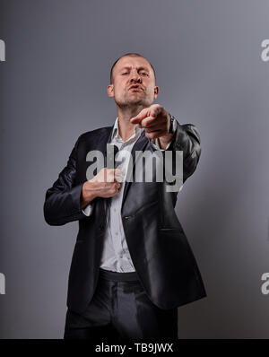 Fun emotional moving happy performer man presenting the show holding microphone in hand and showing the finger the choosing sign on grey color backgro Stock Photo