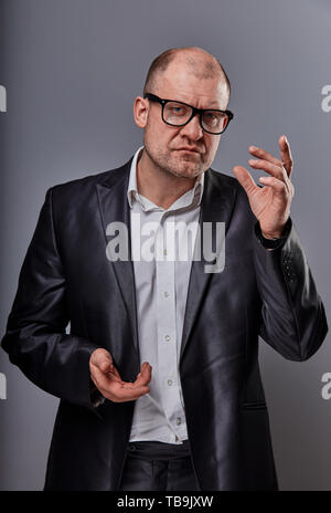 Thinking serious bald business man in eyeglasses and suit discussing and have an idea on grey background. Closeup portriat Stock Photo