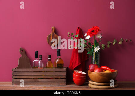 Wooden box with bottles of oil and apples on table near color wall Stock Photo