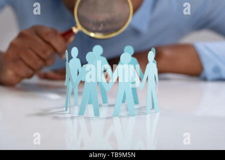 Close-up Of Businessperson Holding Magnifying Glass Over The Human Figures Forming Circle Stock Photo
