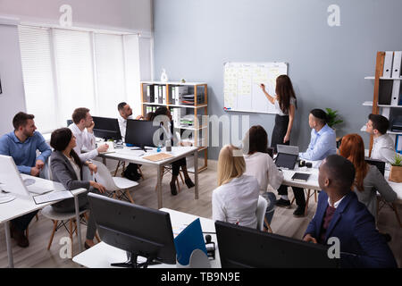Smiling Young Businesswoman Giving Presentation To Her Executives At Workplace Stock Photo